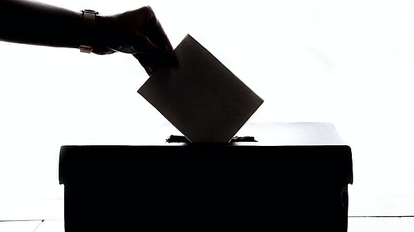 Picture of someone placing a ballot in a ballot box.