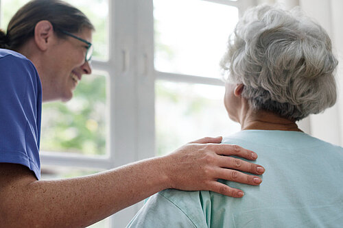 Woman in scrubs with hand on shoulder of older woman